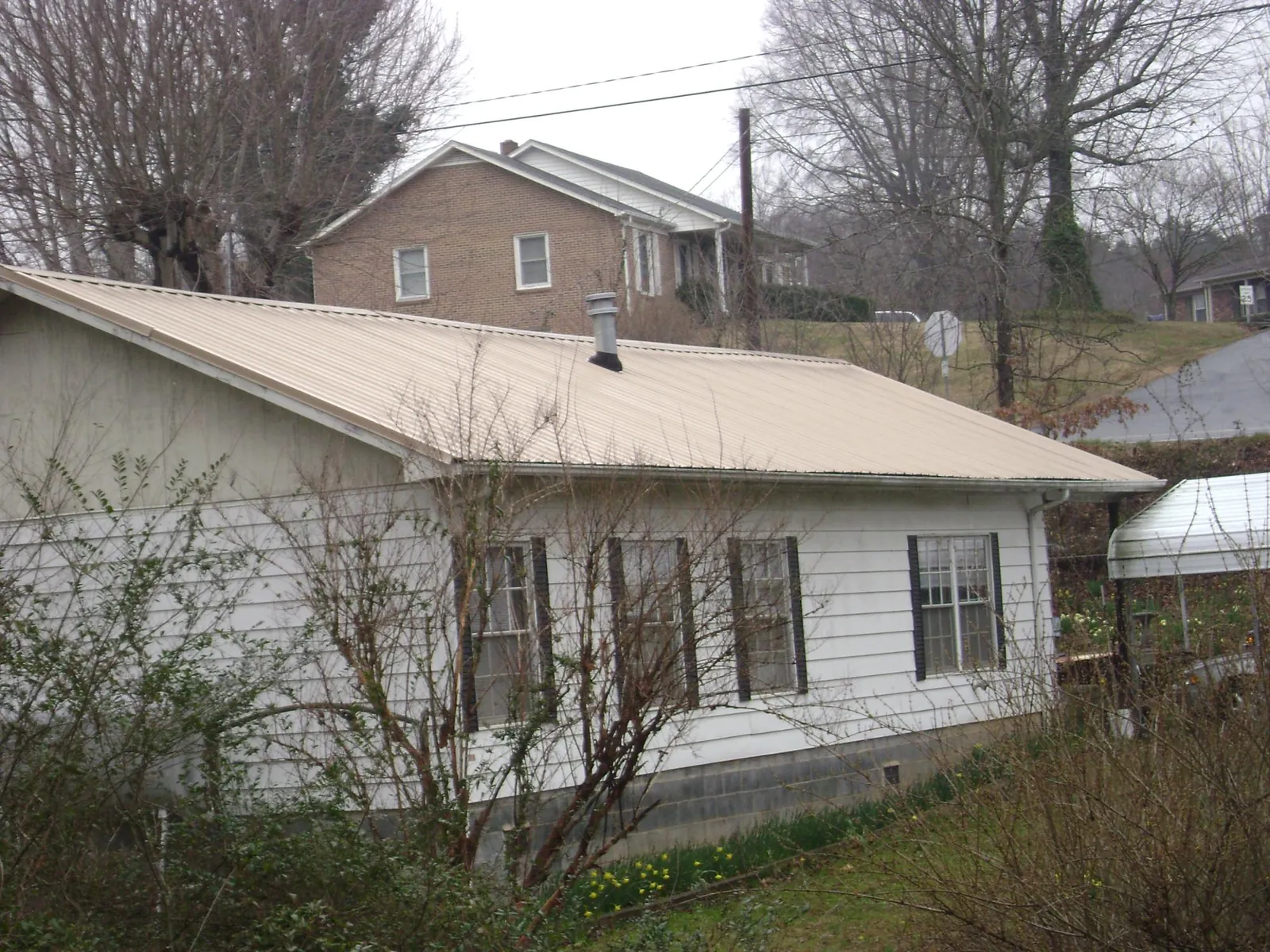 Tan metal roof on a white sided house set into a hillside — Commercial Roofing by Roofing Brothers in Austin